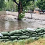 Post-fire flooding showing sand bags and a street that looks like a river, it is full of muddy water.