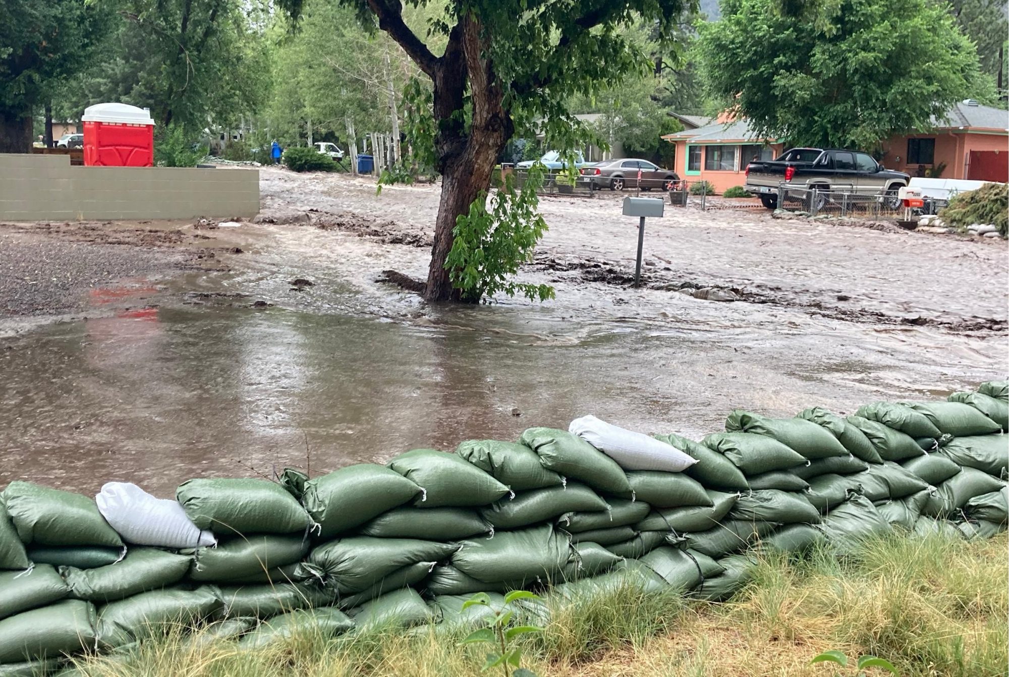 Post-fire flooding showing sand bags and a street that looks like a river, it is full of muddy water.