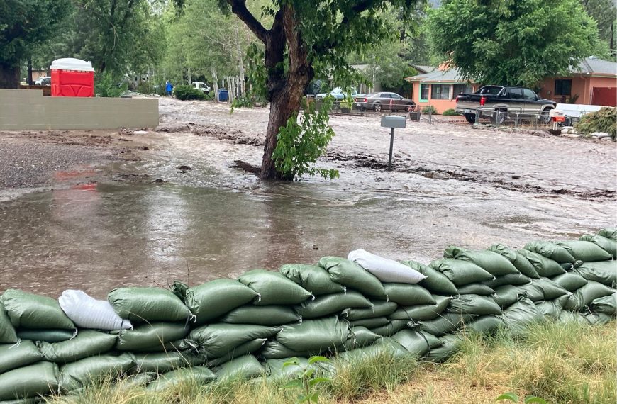 Post-fire flooding showing sand bags and a street that looks like a river, it is full of muddy water.