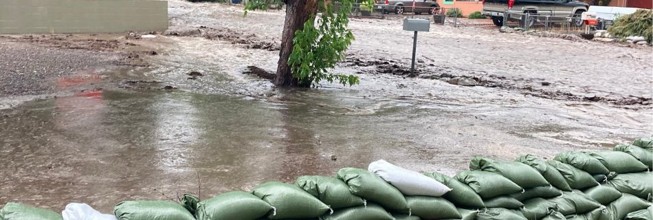 Post-fire flooding showing sand bags and a street that looks like a river, it is full of muddy water.